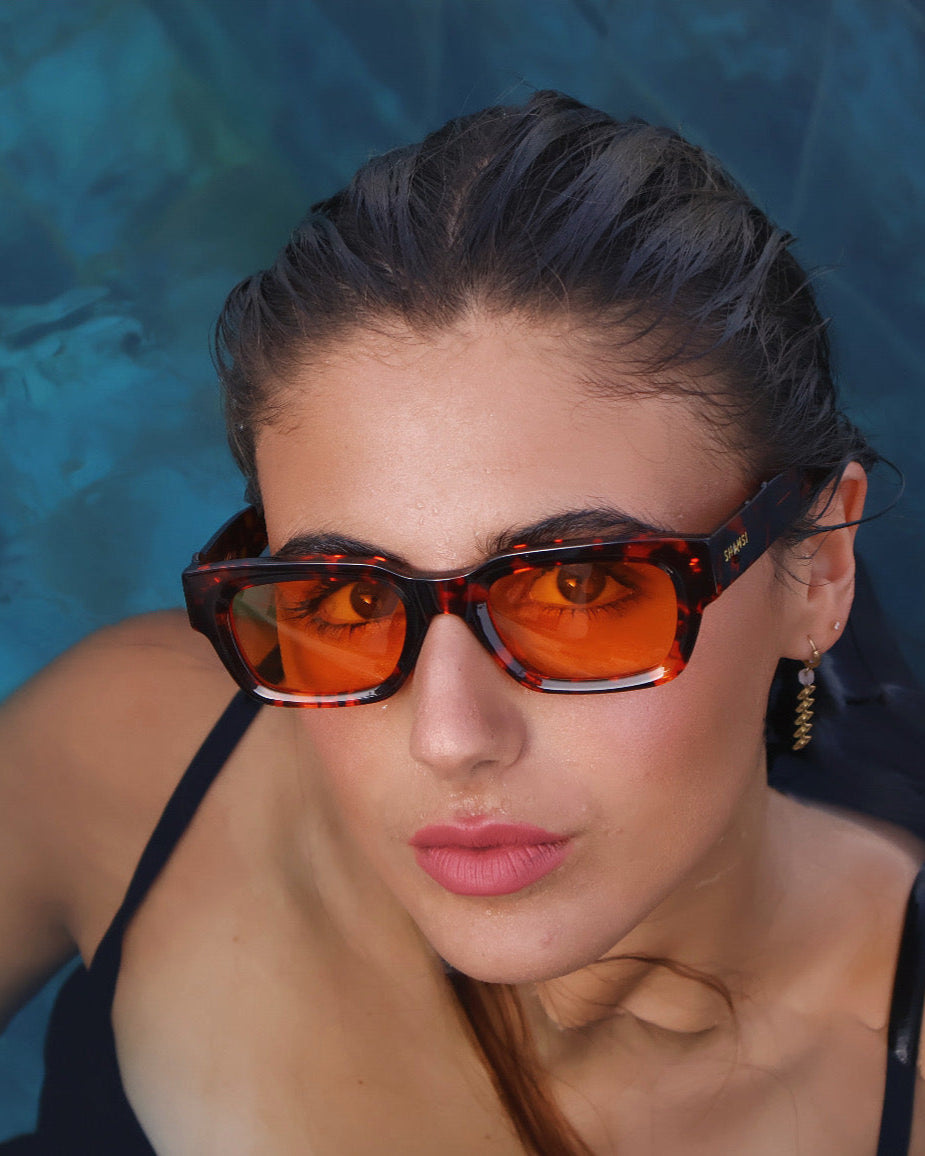 Woman wearing orange-tinted sunglasses with a blue background