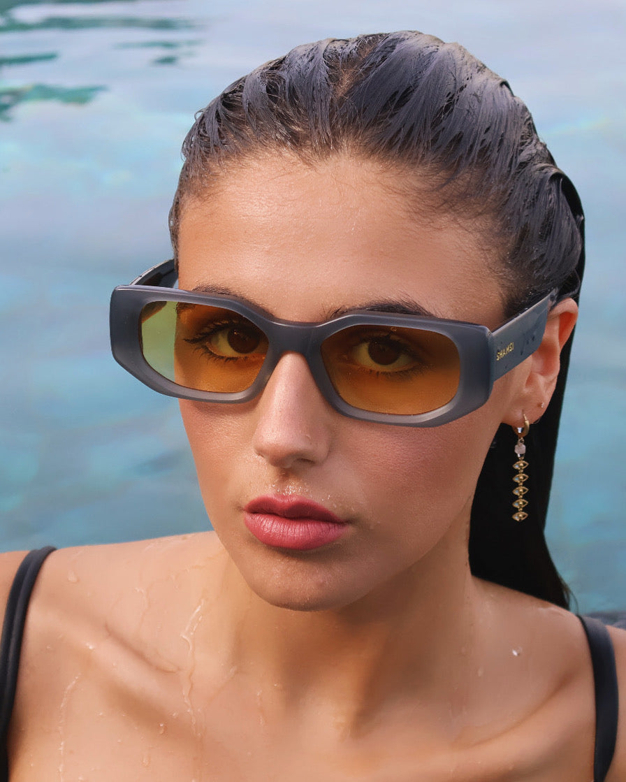 Woman wearing futuristic sunglasses with a blurred water background