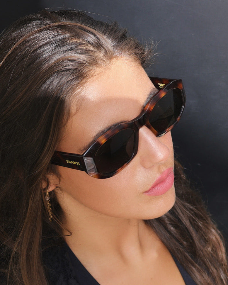 Close-up of a woman wearing tortoiseshell sunglasses with a dark background