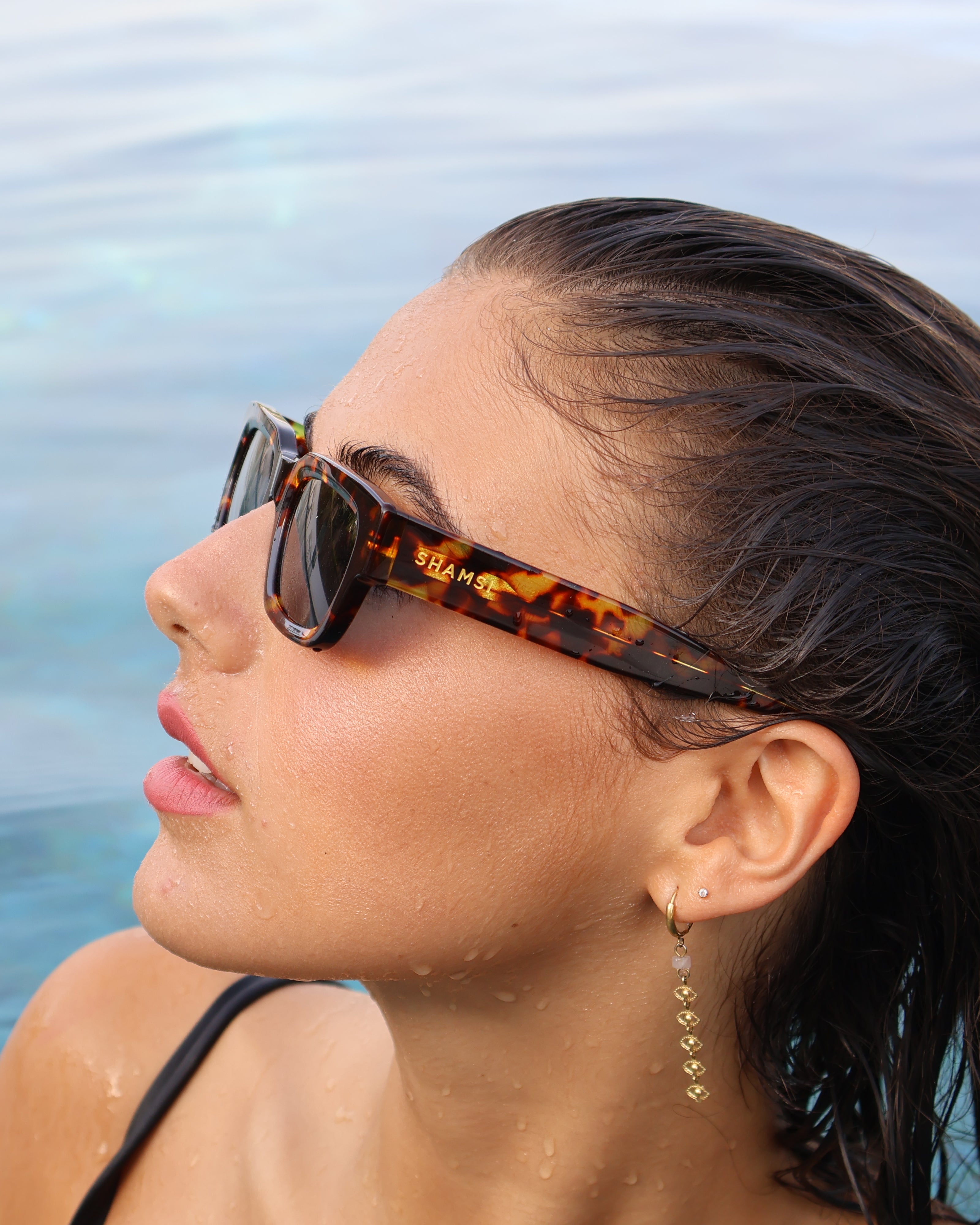 Woman wearing tortoiseshell sunglasses with a blurred ocean background