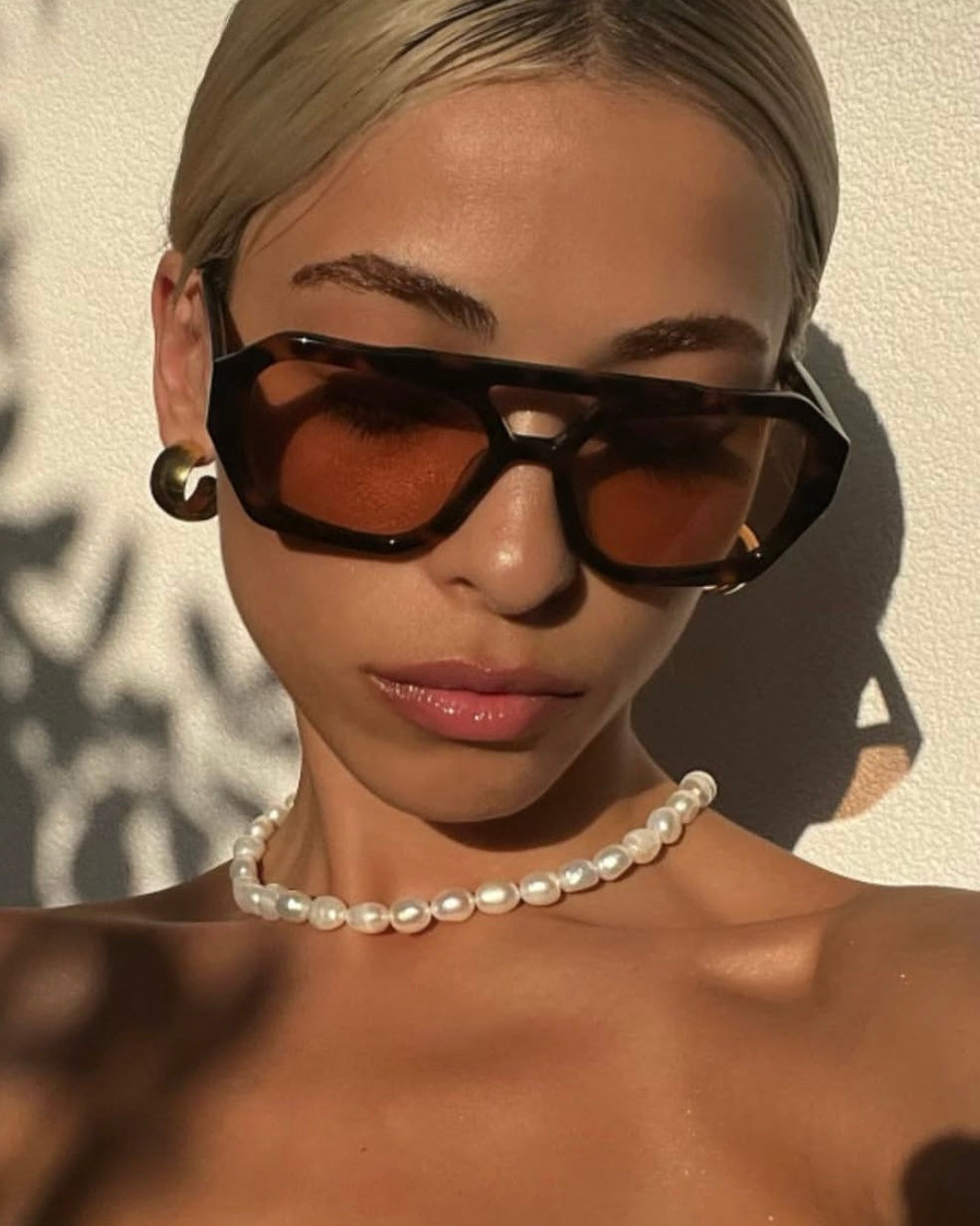 Woman wearing sunglasses and a pearl necklace with a neutral background