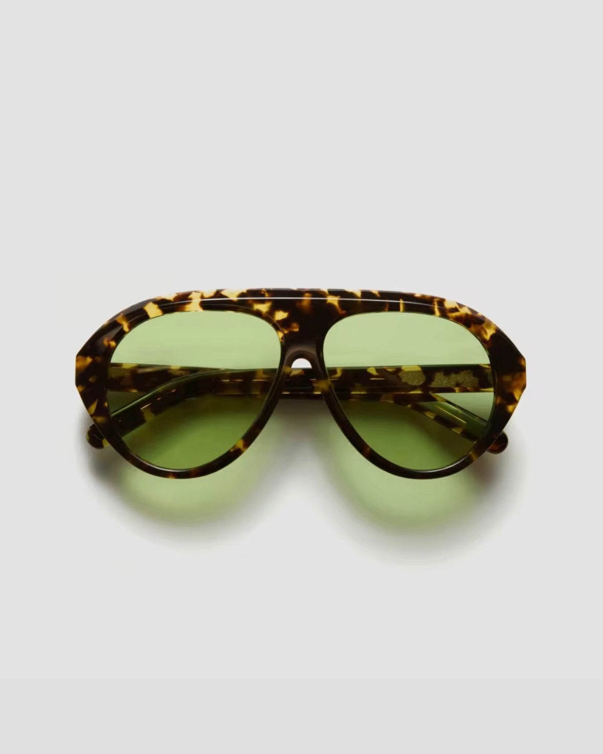 Sunglasses with tortoiseshell frame and green lenses on a light gray background